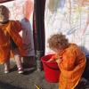 To barnehagebarn i oransje kitlar lagar veggmåleri.