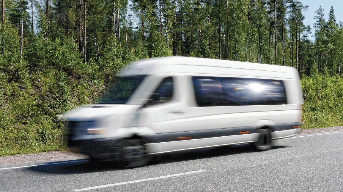 Minibuss køyrer på veg med grøn skog i bakgrunnen - Klikk for stort bilete