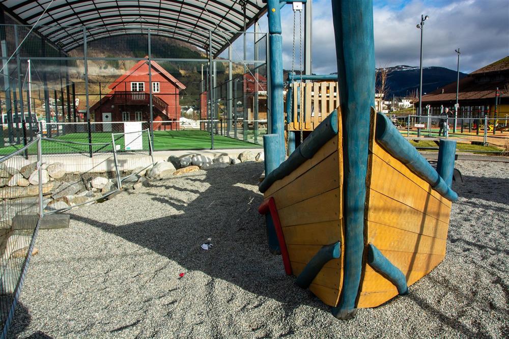 Strand med leikebåt og padelbanen i bakgrunnen. - Klikk for stort bilete